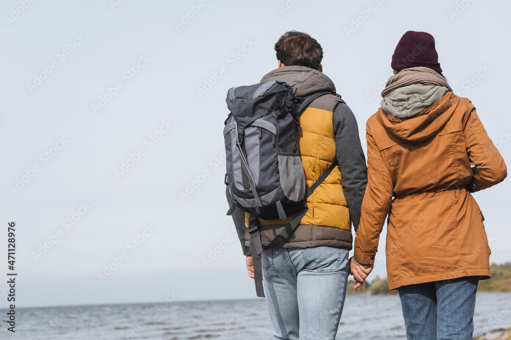 back view of couple in autumn outfit holding hands while hiking near river