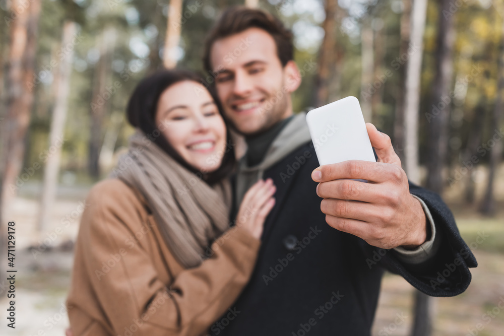 blurred and happy couple taking selfie on smartphone while walking in autumn forest blurred and happy couple taking selfie on smartphone while walking in autumn forest