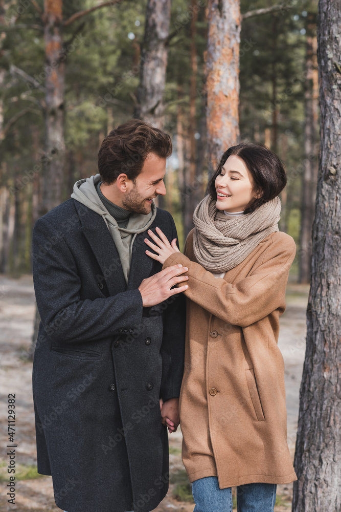 young couple in autumn coats smiling while walking in forest young couple in autumn coats smiling while walking in forest