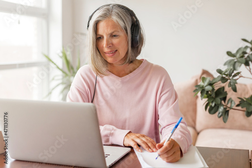 Middle aged businesswoman using earphone while sitting behind her laptop