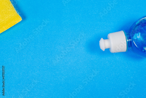 Detergent in a plastic bottle and a sponge (brush) for cleaning the room on a blue background with a place for text (copy space).