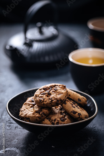 Chocolate chip cookies with tea in background in a dark moody atmosphere 