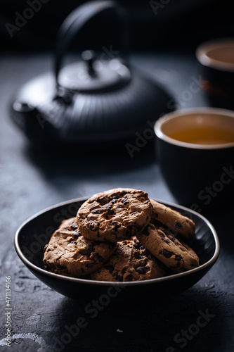 Chocolate chip cookies with tea in background in a dark moody atmosphere 