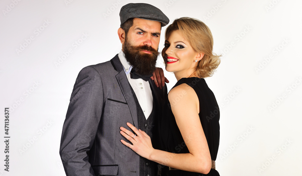 Elegant couple in fashionable clothes hugging. Serious bearded man in suit and smiling woman in black dress.