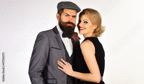 Elegant couple in fashionable clothes hugging. Serious bearded man in suit and smiling woman in black dress.