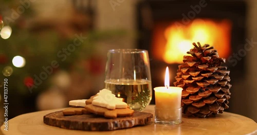 Cozy evening with glass of wine, candles, fire, pine cone and fire with Christmas tree in the background.