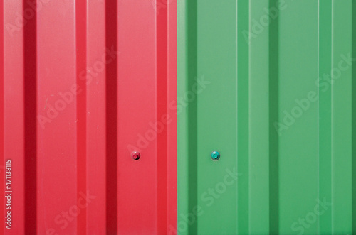 Two sheets of a metal roof of red and green color  extruded by vertical stripes  docked side by side  fixed with roofing screws. Industrial  construction background.