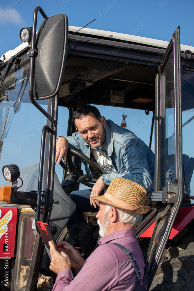 Naklejka premium Two farmers talking beside tractor in field