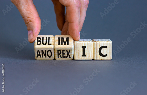Bulimic or anorexic symbol. Doctor turns wooden cubes and changes the word anorexic to bulimic. Beautiful grey table, grey background, copy space. Medical, bulimic or anorexic concept. photo