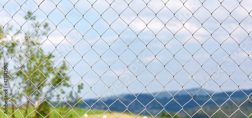 Beautiful plains landscape behind a metal net fence, confinement, prison and imprisonment, quarantine, enclosure area, lockdown simple symbolic abstract concept, nobody, wide banner background shot
