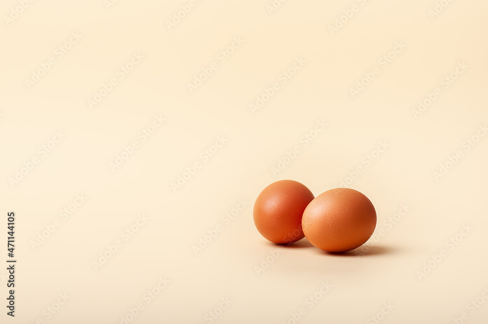 Two brown chicken eggs on pale yellow background with place for text 