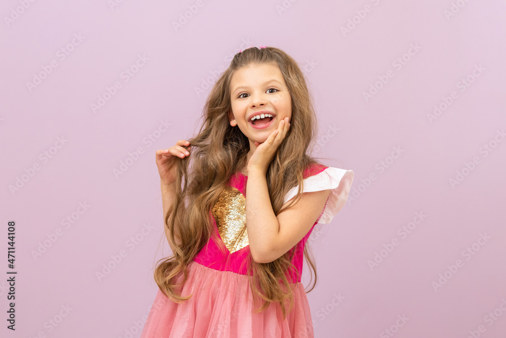 The little girl fluffs her curly, luxurious hair and smiles broadly. Isolated pink background. The little girl fluffs her curly, luxurious hair and smiles broadly. Isolated pink background.