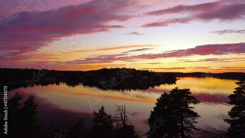 Amazing Beautiful sunset on the Baltic Sea. Bright golden orange pink purple tones of the sunset sky. Rocky Islands of Stockholm archipelago covered with evergreens. Villas on the other coast shore.