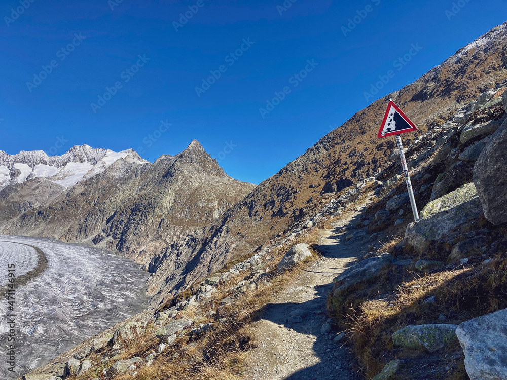 Hiking path along the aletsch glacier with a sign warning of falling stones, Switzerland