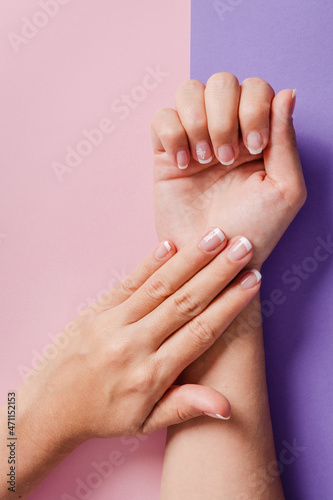 Close-up of woman s hands with French manicure on purple and salmon background.