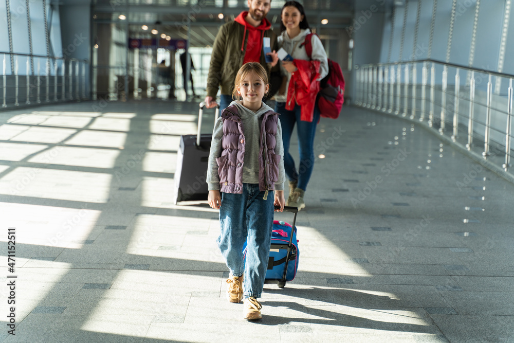 Full length shot of the family of three walking along the airport while carrying their luggages while hurrying up and trying not to miss his flight