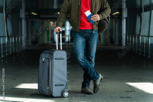 Cropped view of the male tourist is ready for journey. He is standing at the airport and carrying his suitcase. Man is holding his passport © NFstock