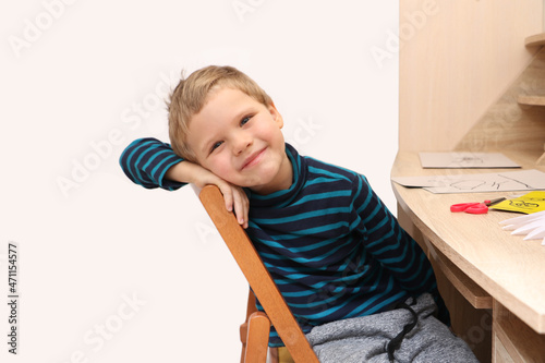 Cute smiling preschool boy sitting at the table.Home education concept or development activities.Online learning.Isolated on white.