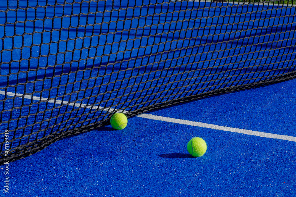 Two balls next to the net of a paddle tennis court. Racket sport concept.