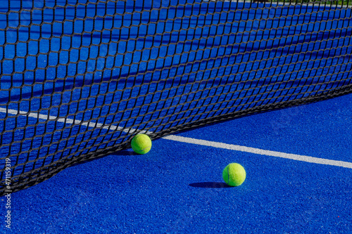 Two balls next to the net of a paddle tennis court. Racket sport concept. © Vic