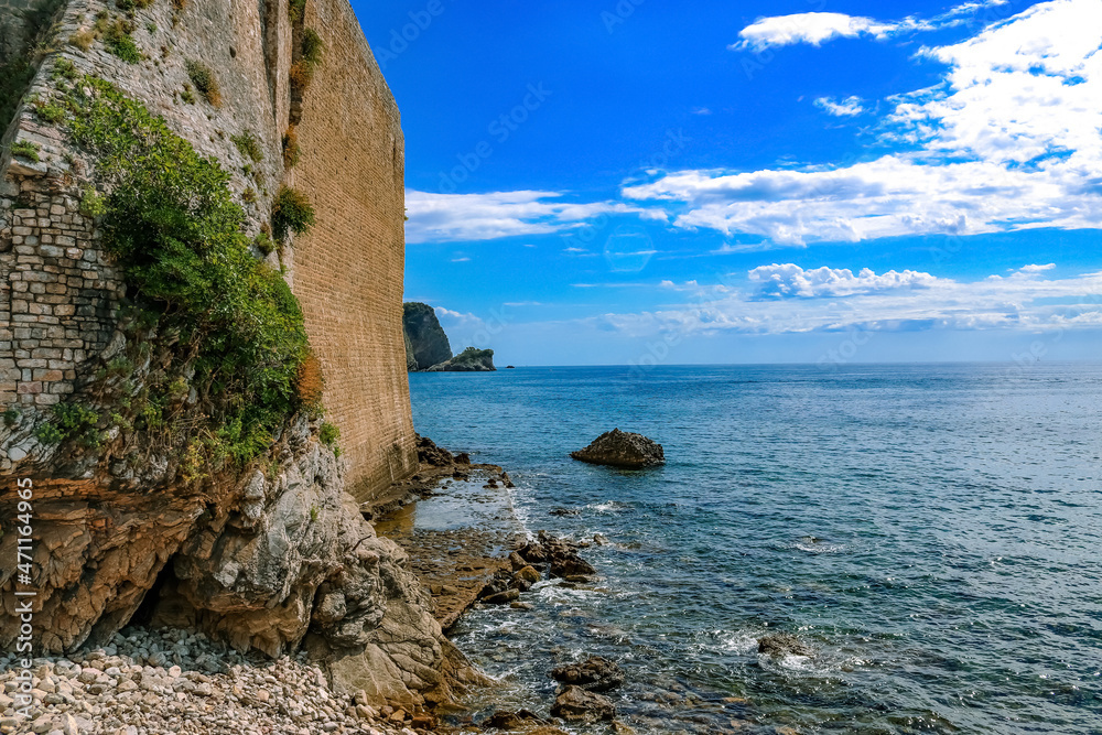 Fototapeta premium Beautiful sea view in the city of Budva. Old stone wall with moss, stones, sky with clouds. Montenegro, Balkans. Summer.
