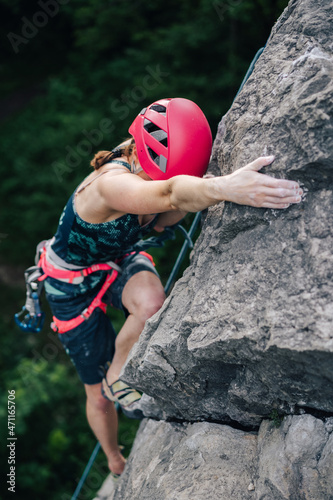 A climber climbing a rock. Woman climber rock climbing steep wall. Adventure sport activity, adrenaline. Girl climbing with a rope, helmet and other rock climbing equipment.