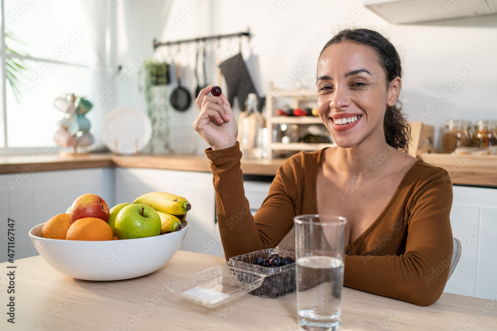 Portrait of Latino attractive woman holding fruits in kitchen at home.