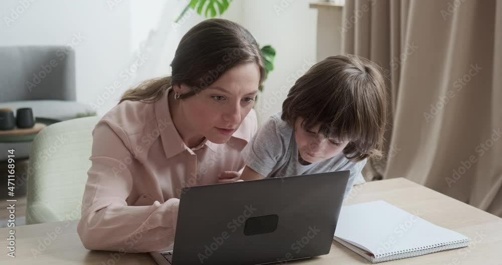 Mom and son are shopping together online using laptop, choosing new toys and gifts. Cute boy whispers his secrets in his ear, trusting his parents. Online schooling learning at home. Mom and son are shopping together online using laptop, choosing new toys and gifts. Cute boy whispers his secrets in his ear, trusting his parents. Online schooling learning at home.