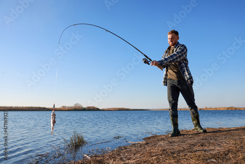 Fisherman catching fish with rod at riverside