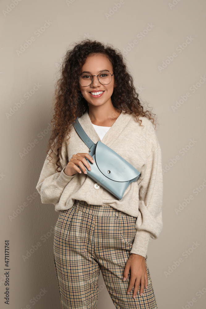 Fototapeta premium Beautiful African American woman with stylish waist bag on beige background