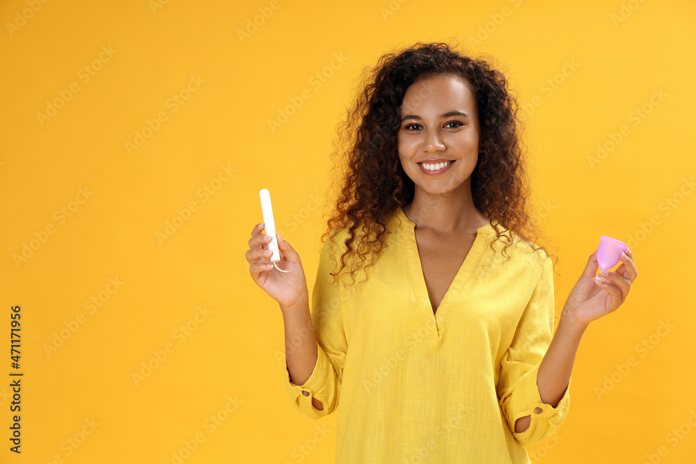 Young African American woman with tampon and menstrual cup on yellow background Young African American woman with tampon and menstrual cup on yellow background