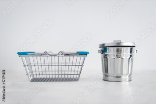 consumerism vs sustainable intentional shopping, shopping basket for good to be purchased next to recycling bin for excess goods being produced or bought photo