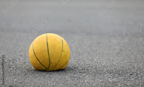 Left hand focus, old tired deflated let down yellow basketball on a road surafce concept. needs air, worn out spent and discarded sport equipment. photo