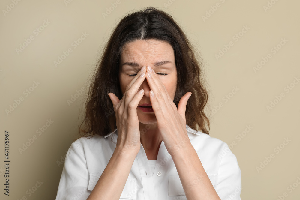 Mature woman suffering from headache on beige background Mature woman suffering from headache on beige background