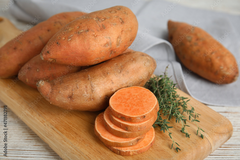 Wooden board with thyme and sweet potatoes on table, closeup Wooden board with thyme and sweet potatoes on table, closeup