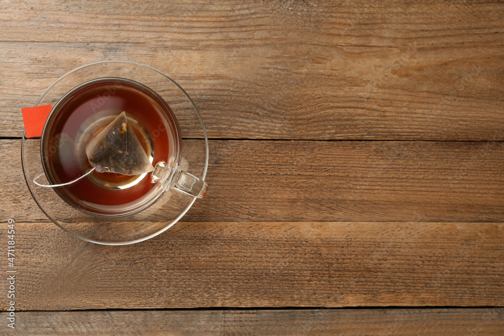 Tea bag in glass cup of hot water on wooden table, top view. Space for text Tea bag in glass cup of hot water on wooden table, top view. Space for text