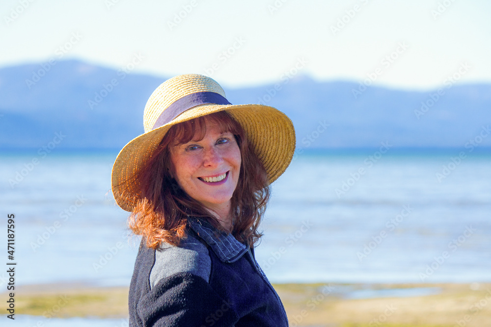 A portrait of a beautiful senior woman smiling and enjoying her contented life in front of a mountain lake while on vacation.