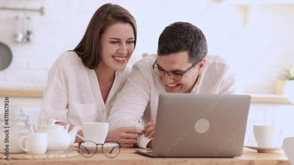 Closeup view of young couple looking at laptop screen and laughing, sitting at table in home spbi. Front view of beautiful woman, man watch video or web on computer screen and talk with smiles, laugh Closeup view of young couple looking at laptop screen and laughing, sitting at table in home spbi. Front view of beautiful woman, man watch video or web on computer screen and talk with smiles, laugh