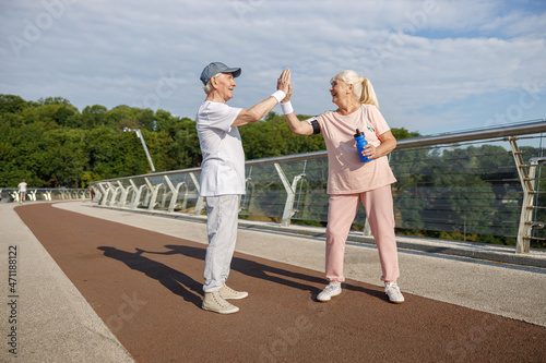 Joyful senior man and woman in sportswear give five training together on footbridge