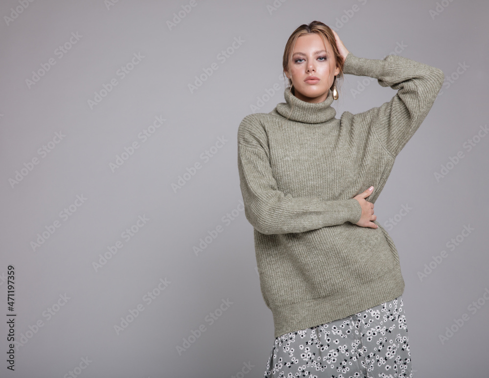 Fashion photo of a beautiful elegant young woman in a pretty pale green sweater, gray long skirt with patterns, white boots posing over light gray background. Studio shot, portrait. Monochrome colors Fashion photo of a beautiful elegant young woman in a pretty pale green sweater, gray long skirt with patterns, white boots posing over light gray background. Studio shot, portrait. Monochrome colors