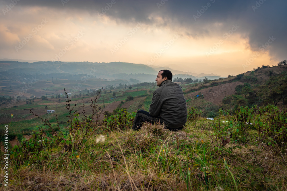 young man sitting on mountain top with misty hill range background and dramatic sky at morning young man sitting on mountain top with misty hill range background and dramatic sky at morning
