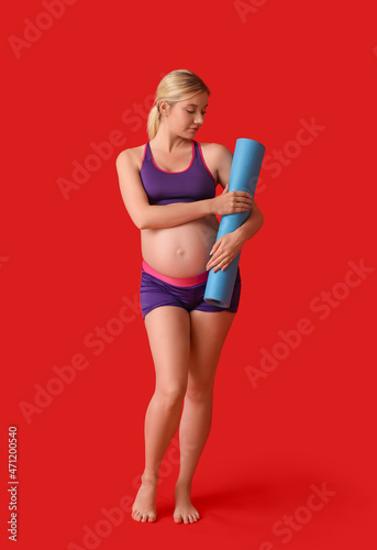 Young pregnant woman with yoga mat on red background