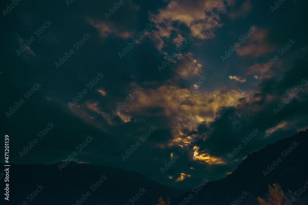 Naklejka premium The orange full moon rising from behind the mountain range illuminates the misty clouds, creating a mystical atmosphere. supermoon.the rising moon in the gorge of the Caucasus Mountains. long exposure
