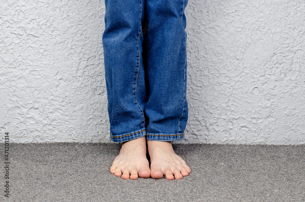 Child's bare feet. Child's legs in jeans. Sitting on the floor. Child's bare feet. Child's legs in jeans. Sitting on the floor.