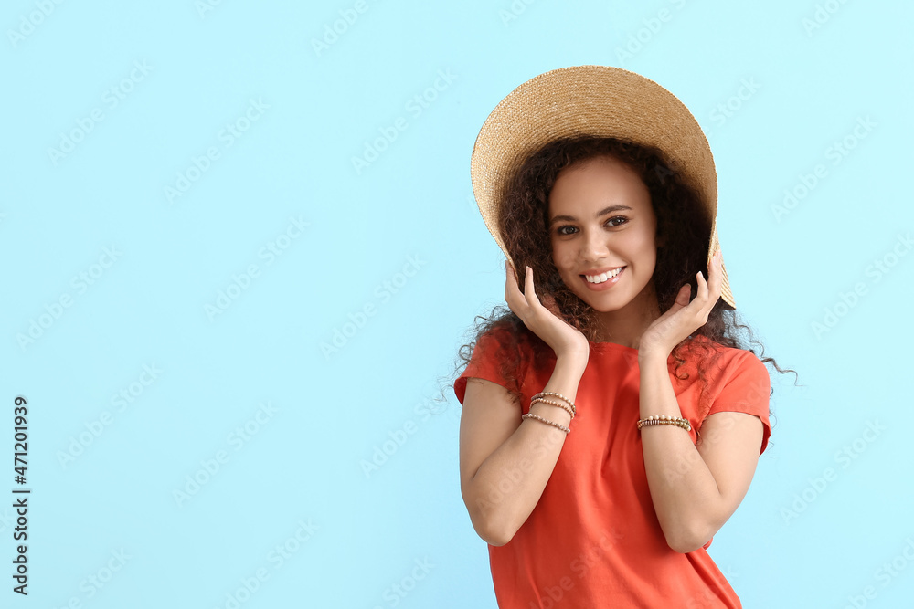Beautiful African-American woman in broad brim hat on color background