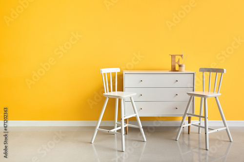 Modern chairs and chest of drawers near color wall