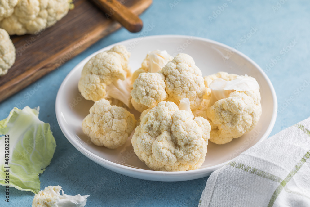 Raw cauliflower slices in a light bowl on a blue background with copy space. Raw cauliflower slices in a light bowl on a blue background with copy space.