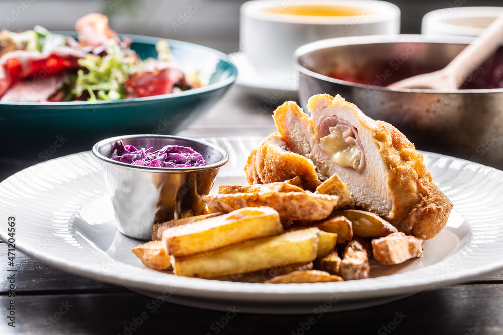 Chicken cordon bleu with ham and cheese inside served with fried potato wedges and red cabbage salad Chicken cordon bleu with ham and cheese inside served with fried potato wedges and red cabbage salad