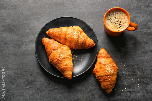 Plate with delicious croissants and cup of coffee on black background