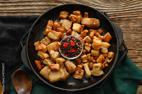 Frying pan with tasty cracklings on wooden background